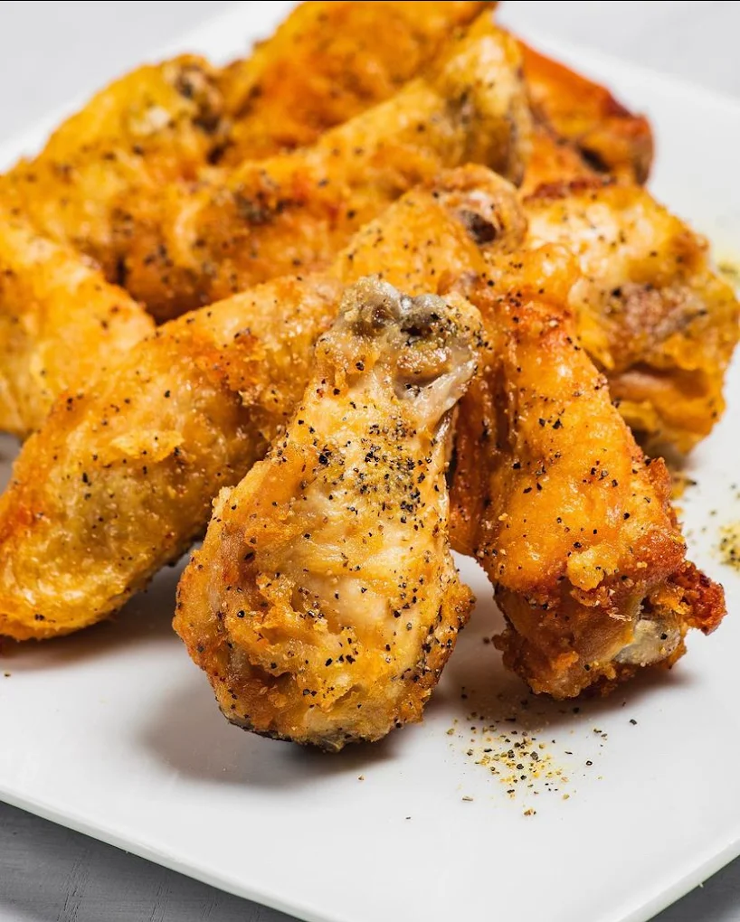 Crispy lemon pepper chicken wings seasoned with black pepper on a white plate at Mo’s in Simsbury.